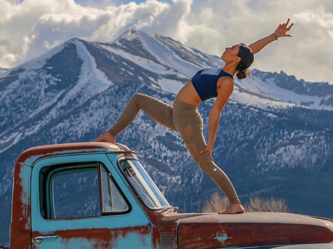 Kelly Pender Reverse Warrior Yoga Pose Standing on Red Car with Mountain in background