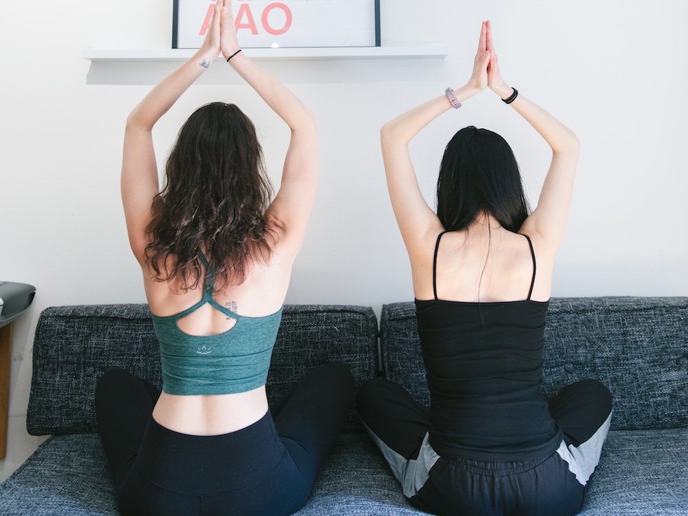 Two girls in yoga attire practicing with anjali mudra overhead practicing meditation