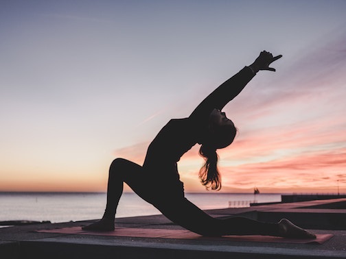 Female doing low lunge yoga pose with sunset background